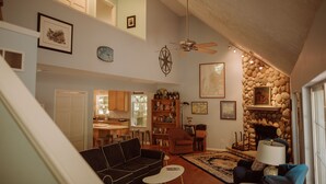 A spacious living room with a high ceiling, a fireplace, a bookshelf, and a dining area. - Cedar Point Cottage- Perfect Lake Michigan Retreat (Mears)
