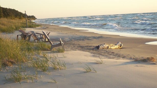 A beach with two wooden lounge chairs and a large rock formation. - Cedar Point Cottage- Perfect Lake Michigan Retreat (Mears)
