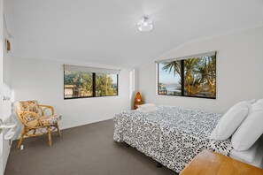 A bedroom with a bed, two windows, a chair, and a small table.
