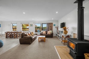 A modern living room with a fireplace, sofas, a coffee table, and a dining area. - ACCOMMODATE 19 - OCEAN FRONT. (Pukehina)