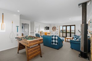 A modern living room with a foosball table, sofas, a fireplace, and a large window.