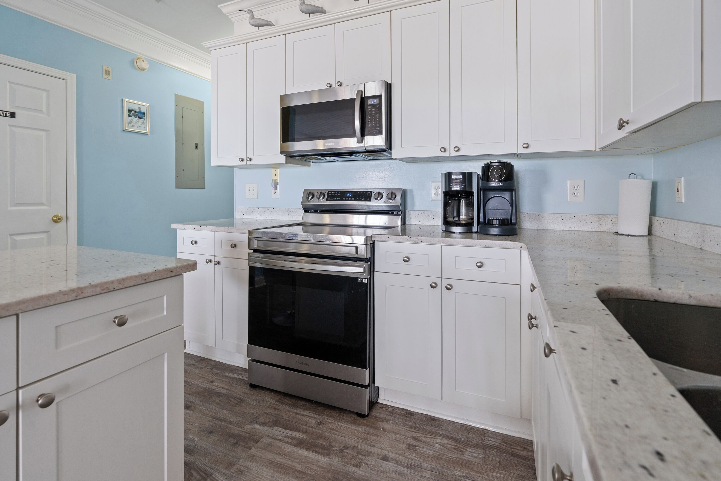 A kitchen with white cabinets, a stainless steel microwave, a built-in oven, and a coffee maker.