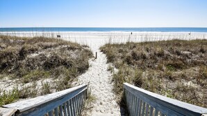 Un sentier de sable qui longe la plage et mène à l’océan, avec des garde-corps en bois de chaque côté.
