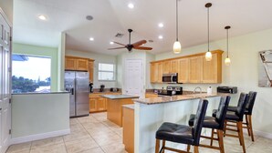 A modern kitchen with a central island, wooden cabinets, stainless steel appliances, and pendant lighting. -   160 inch pool tv plus 120 inch great room tv  6 Bed  5 Bath Pool and hot tub (Fort Myers Beach)