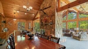 A spacious wooden dining area with a stone fireplace, large windows, and a cozy seating area with a couch and chairs. - Repeat Retreat — Your Place to Come Back To! (Lake Harmony)