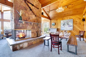A cozy interior with a stone fireplace, wooden ceiling, and a dining area.
