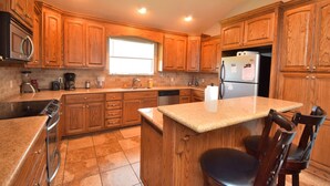 A kitchen with wooden cabinets, a granite countertop, a refrigerator, and a window.