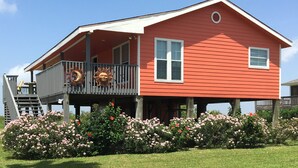 A red house with a balcony, a wooden deck, and a garden with pink flowers.