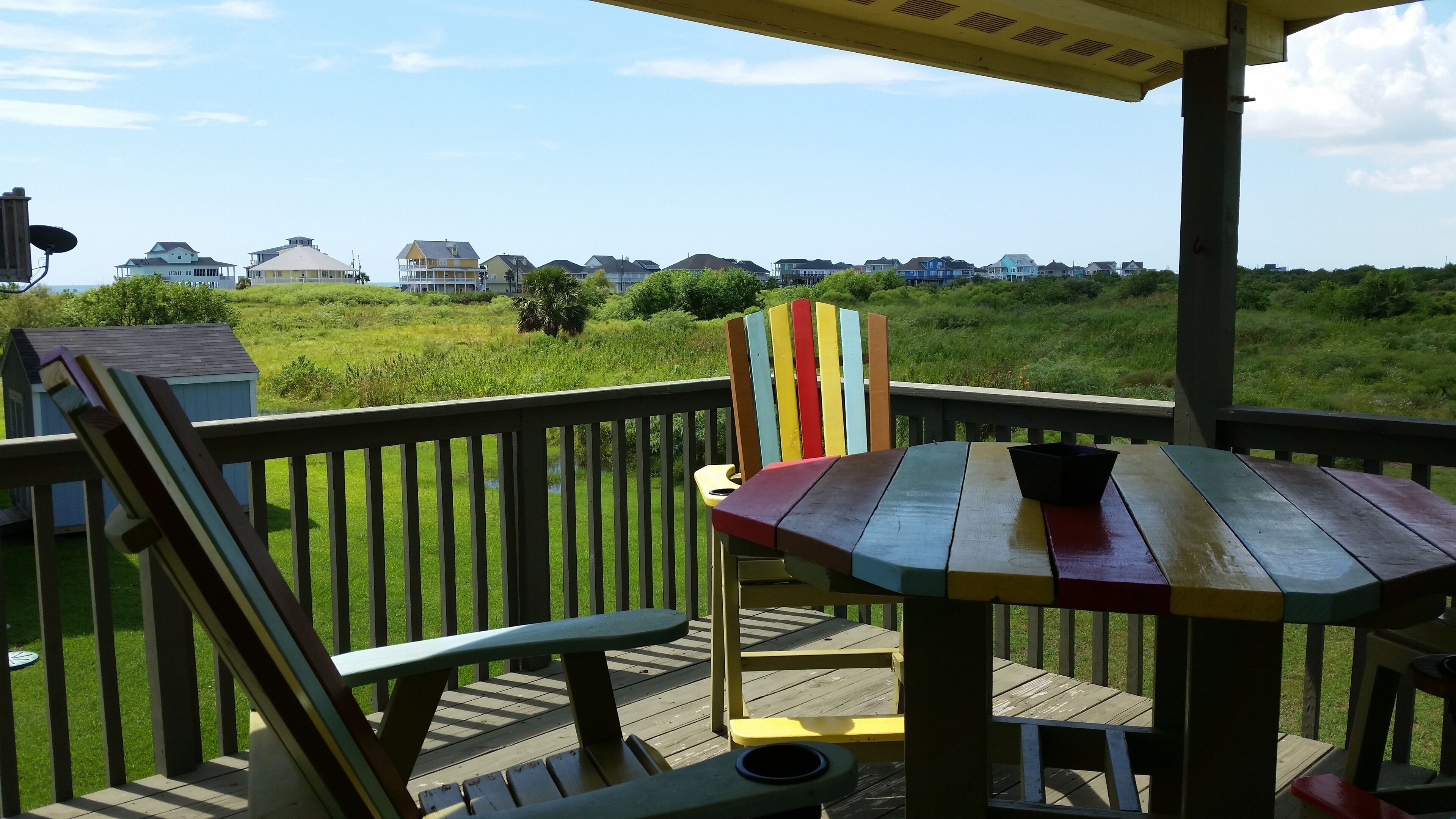 A wooden deck with a table and chairs, overlooking a grassy area with houses in the background.
