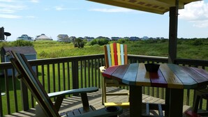 A wooden deck with a table and chairs, overlooking a grassy area with houses in the background.