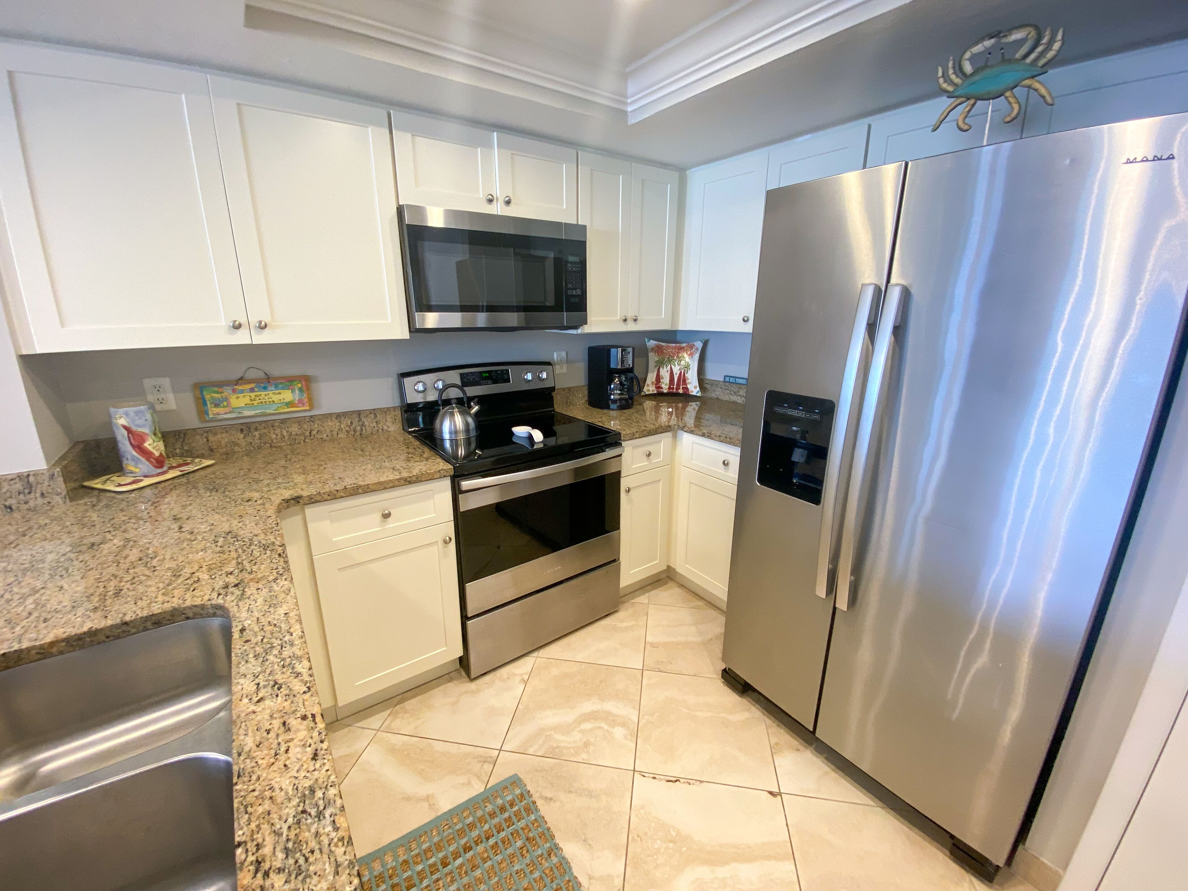 A kitchen with white cabinets, a stainless steel refrigerator, a microwave, an oven, and a coffee maker.