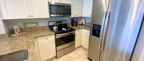 A kitchen with white cabinets, a stainless steel refrigerator, a microwave, an oven, and a coffee maker.
