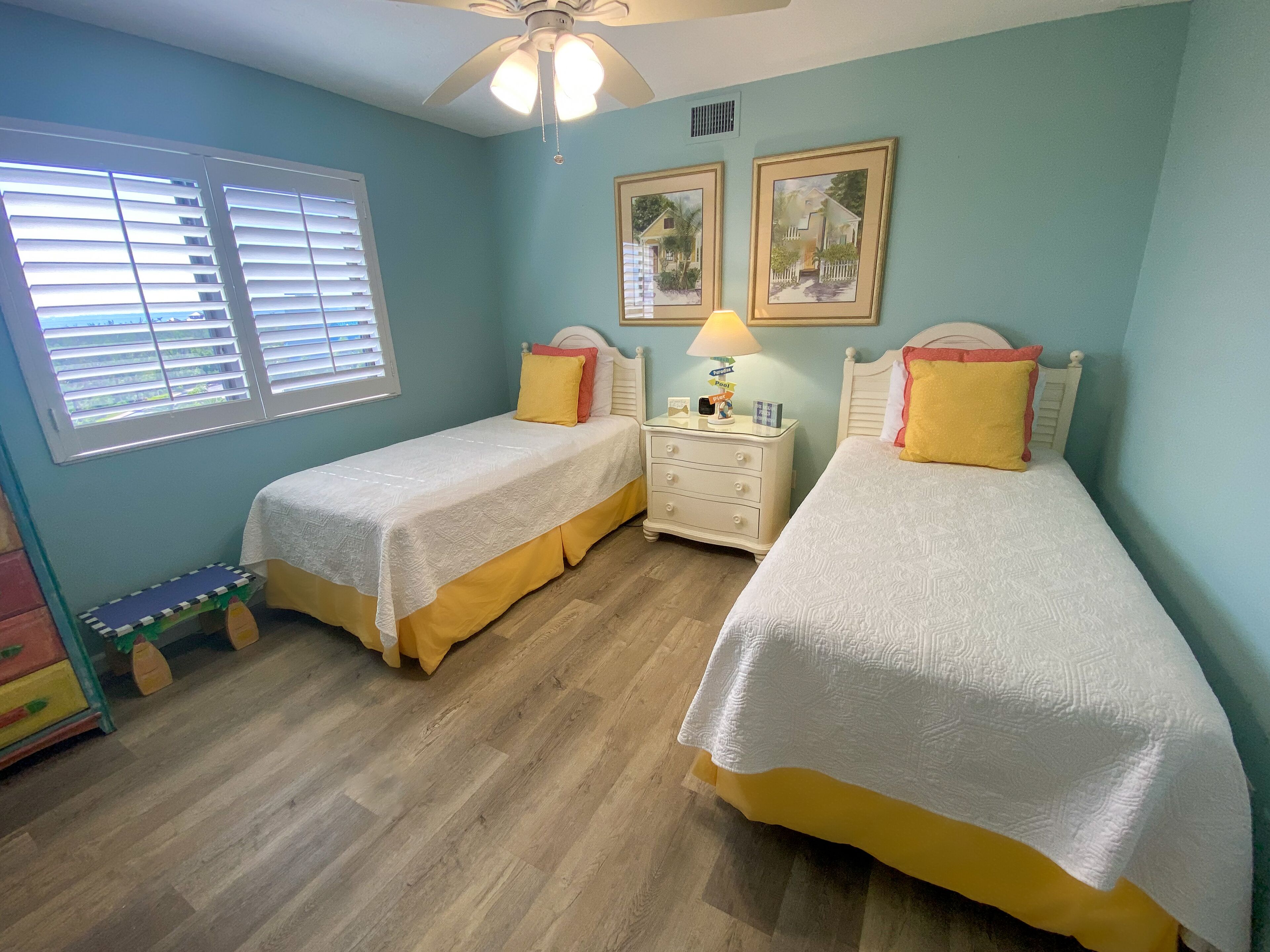 A bedroom with two single beds, a nightstand with a lamp, and a ceiling fan.
