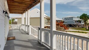 Une terrasse en bois couverte, dotée de rampes blanches, qui mène à une zone résidentielle avec des maisons et un escalier.
