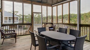 Une terrasse extérieure couverte, dotée d’une table et de chaises, de grandes fenêtres et offrant une vue sur les arbres et une maison.