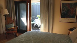A bedroom with a bed, a chair with a cushion, a table with a vase of flowers, and a painting on the wall. - Private En Suite Large Master Bedroom With King Sized Bed   (Burlington)