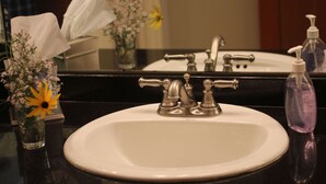 A bathroom sink with a mirror above it, a tissue box, and a small vase with flowers. - Private En Suite Large Master Bedroom With King Sized Bed   (Burlington)