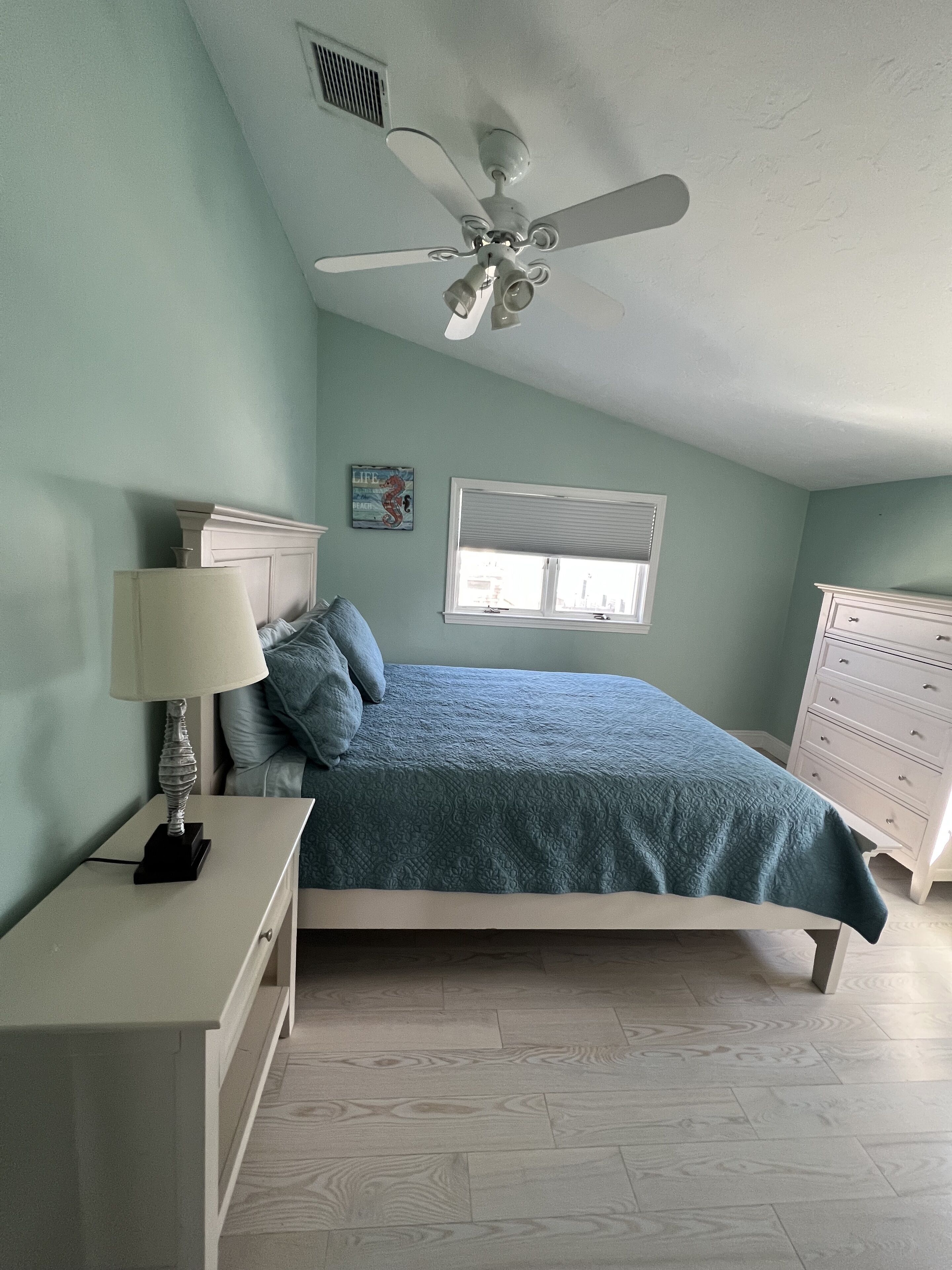 A bedroom with a bed, a nightstand, a dresser, a ceiling fan, and a window.