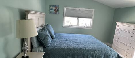 A bedroom with a bed, a nightstand, a dresser, a ceiling fan, and a window.