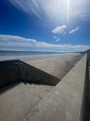 A concrete staircase leading down to a sandy beach with a clear sky and ocean in the background.