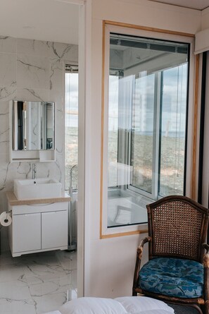 A bathroom with a marble sink, a mirror, and a large window with a view of the beach.