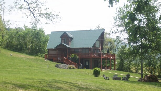 A large log cabin with a green roof, a porch, and a staircase leading to the entrance. - Papa Bear's River Cabin- 3 bedroom, 2 full bath, Riverfront (Shenandoah)