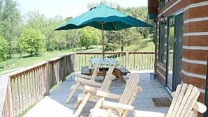 A wooden deck with Adirondack chairs and a table under a green umbrella, overlooking a grassy area. - Papa Bear's River Cabin- 3 bedroom, 2 full bath, Riverfront (Shenandoah)