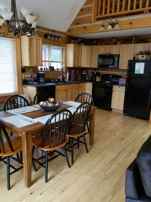 Una cocina tipo cabaña de madera con una mesa y sillas, un refrigerador negro y un microondas.