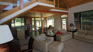 A spacious living area with high ceilings, a kitchen, and large windows.