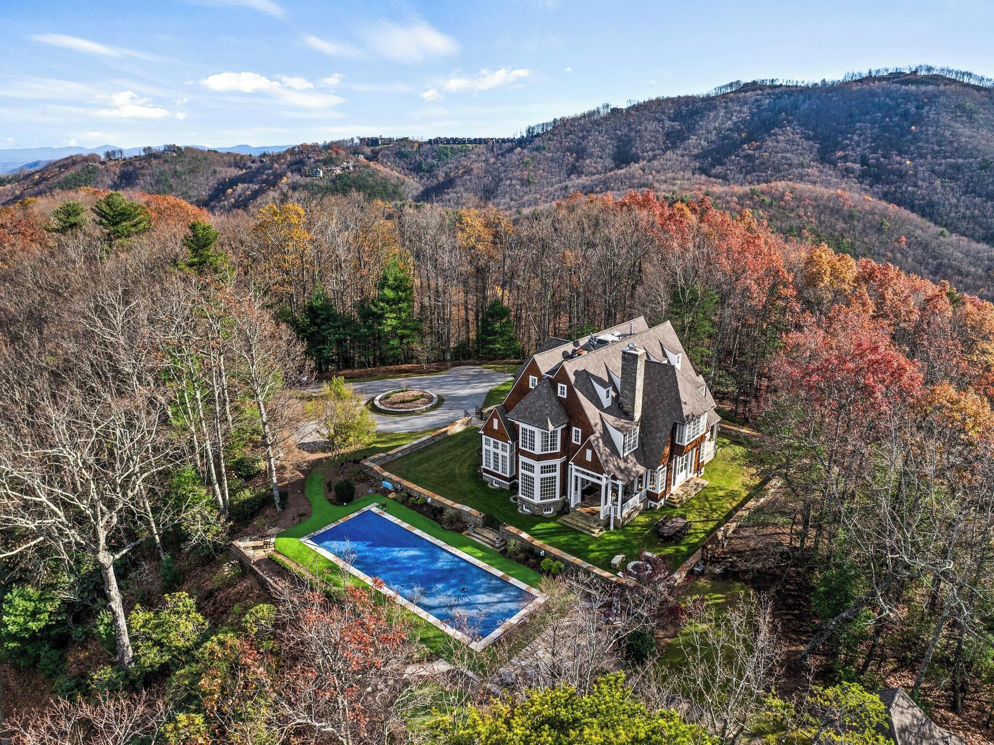 A large, two-story house with a wrap-around porch, a swimming pool, and a well-maintained lawn.