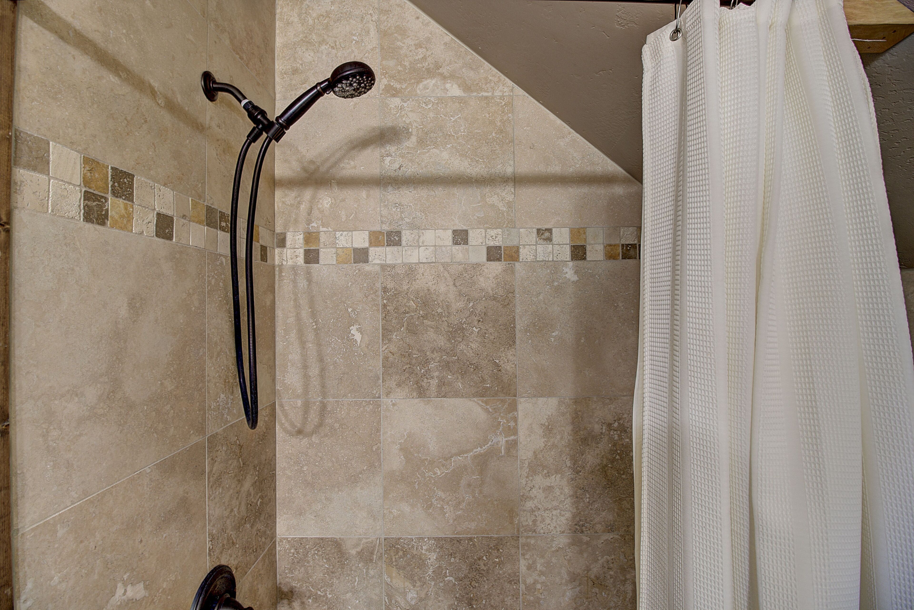A shower area with a handheld showerhead and a white shower curtain.