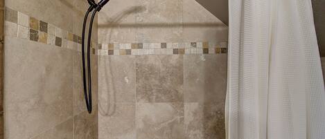 A shower area with a handheld showerhead and a white shower curtain.