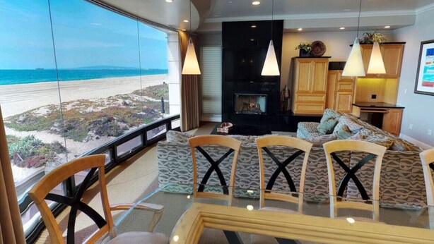 Ein gemütliches Wohnzimmer mit großem Fenster zum Strand, einem Kamin und einem Essbereich mit Stühlen und Tisch.