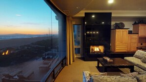 Ein modernes Wohnzimmer mit Kamin, einer Couch und Blick auf den Strand.