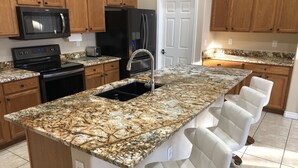 Eine Küche mit Granit Arbeitsplatten, einer Edelstahl-Spüle, einem Kühlschrank, einer Mikrowelle und Holzschränken.