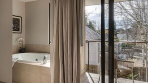 A modern bathroom with a bathtub, a shower, and a large window offering a view of the outdoors.