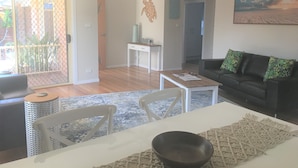 Un salon avec un canapé de couleur foncée, une table à manger blanche et un ventilateur de plafond.