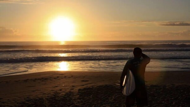 Une scène de plage où une personne se tient face à l’océan au coucher du soleil.
