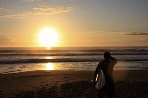 Ein Strandbild mit einer Person, die zum Sonnenuntergang hin zum Meer steht.