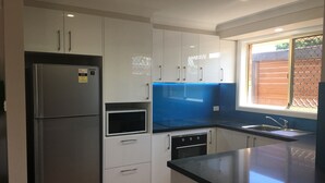 Une cuisine moderne avec des meubles blancs, un réfrigérateur en acier inoxydable, un four à micro-ondes et un évier avec un pare-éclaboussures bleu.