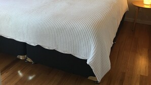 Un lit bien fait, recouvert d’une courtepointe blanche à texture, avec deux oreillers et une tête de lit. Un tableau représentant des pierres empilées est accroché au mur au-dessus du lit.