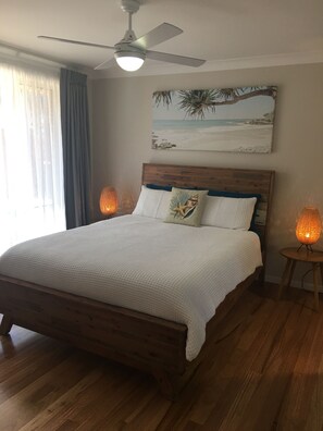 Une chambre à coucher avec un lit en bois, un ventilateur de plafond, un tableau sur le thème de la plage et deux lampes de table.