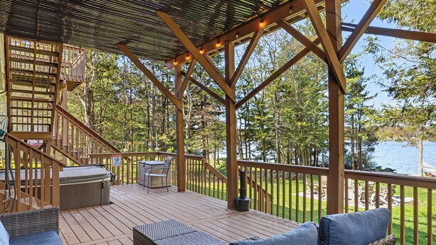 Eine Holzterrasse mit Gartenmöbeln, einem Whirlpool und Blick auf den See.
