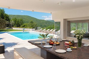 A poolside dining area with a view of a mountain, outdoor seating, and a buffet setup.