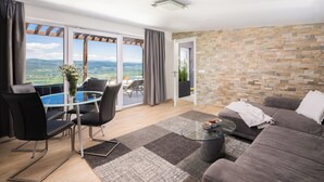Una sala de estar moderna con una mesa de vidrio, sillas negras, un sofá gris y una pared de piedra.