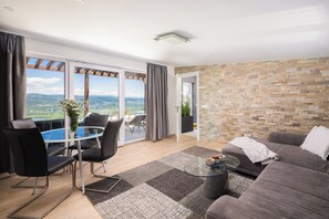 A modern living room with a glass table, black chairs, a grey sofa, and a stone wall.