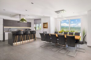 A modern kitchen with a bar area, dining table with chairs, and large windows with a city view.