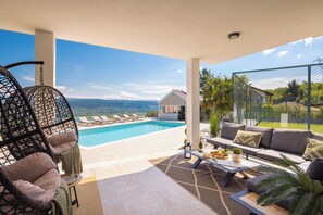 A poolside area with lounge chairs, a sofa, and a table with a bottle and glasses.