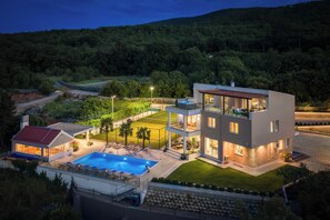 A modern two-story house with a swimming pool, tennis court, and a well-maintained garden.