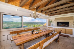 A wooden dining table with benches, a chandelier, a fireplace, and large windows with a view of the landscape.